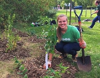 Natalie squatting down next to recently planted tree