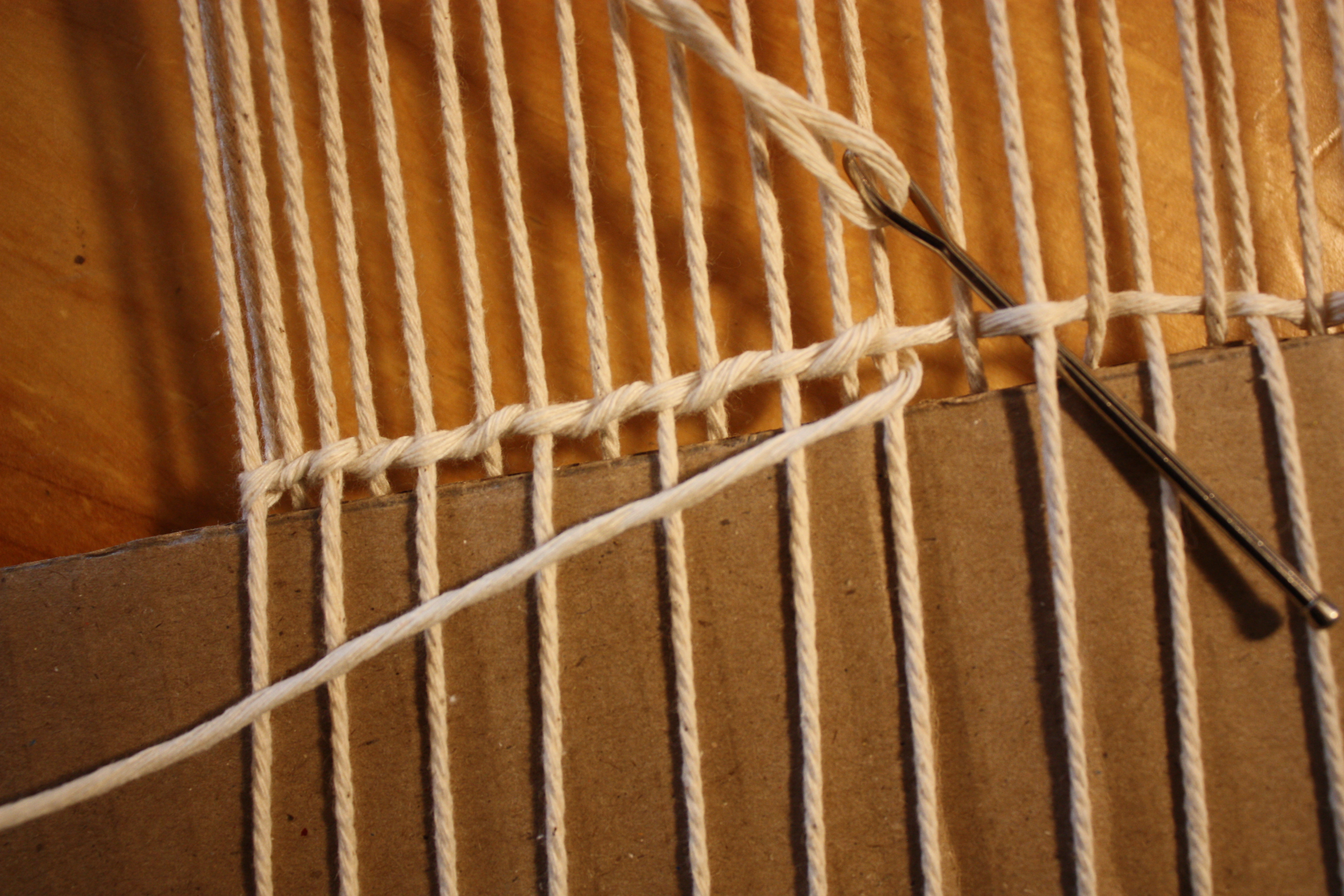 Needle tucking down and behind the warp where the weft sits on top. Where the Weft is being brought forward and crossed to the next warp, showing the “twist.