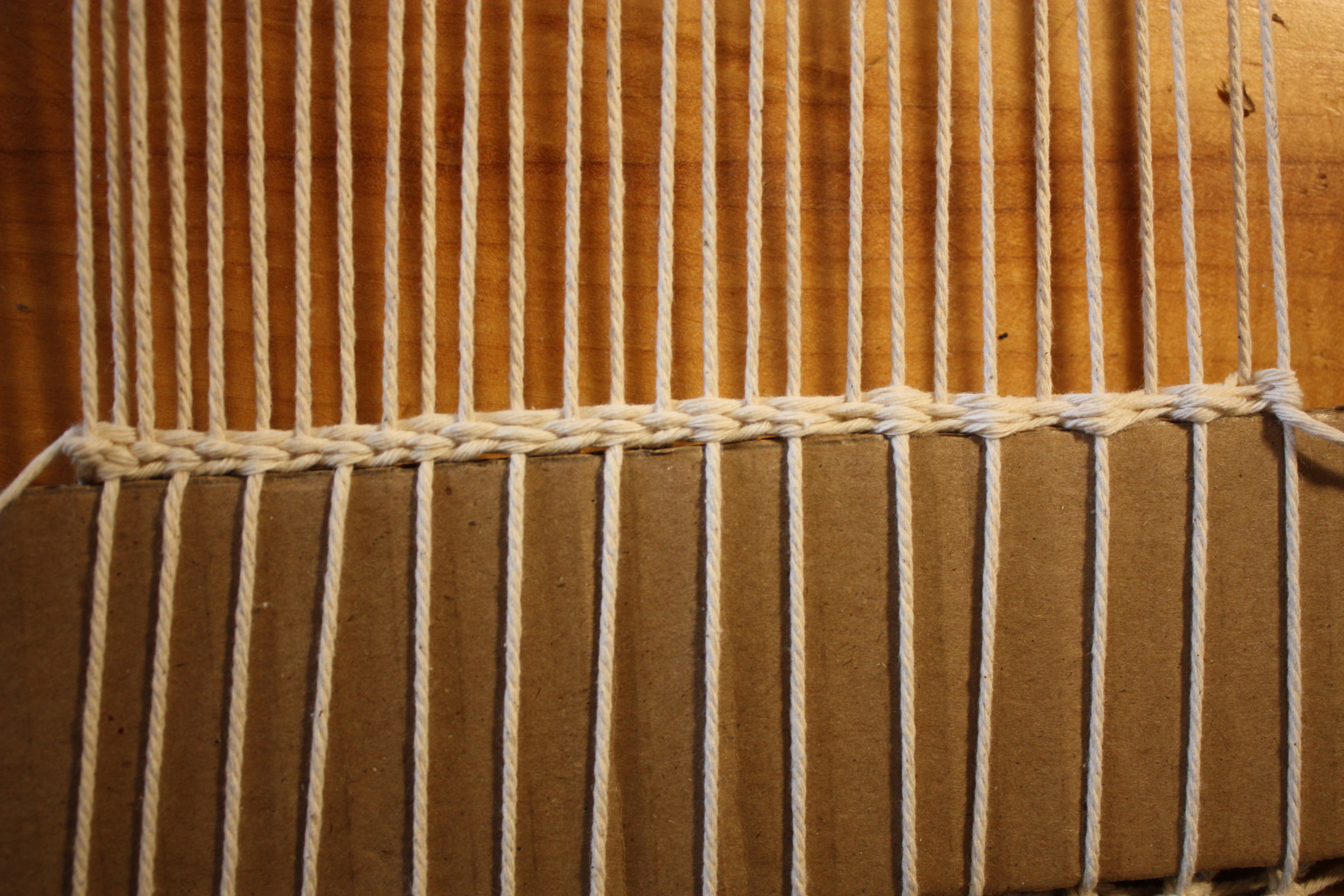 A wide shot showing the completed base: cardstock, one plain weave row, twisting stitch row, and a few more plain weave rows stacked neatly.