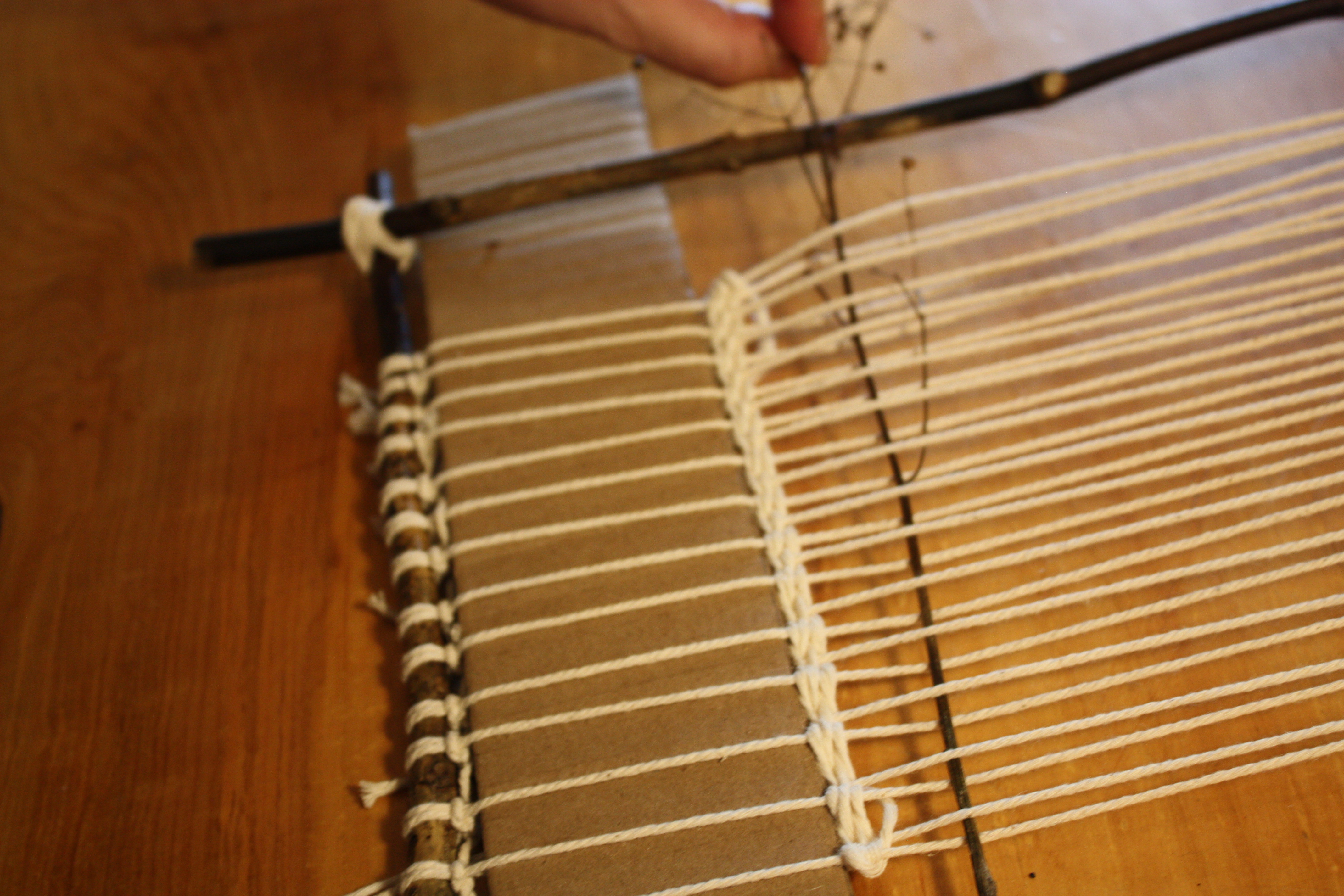  In-progress weaving with natural materials — grasses, twigs, flowers layered between rows of yarn.