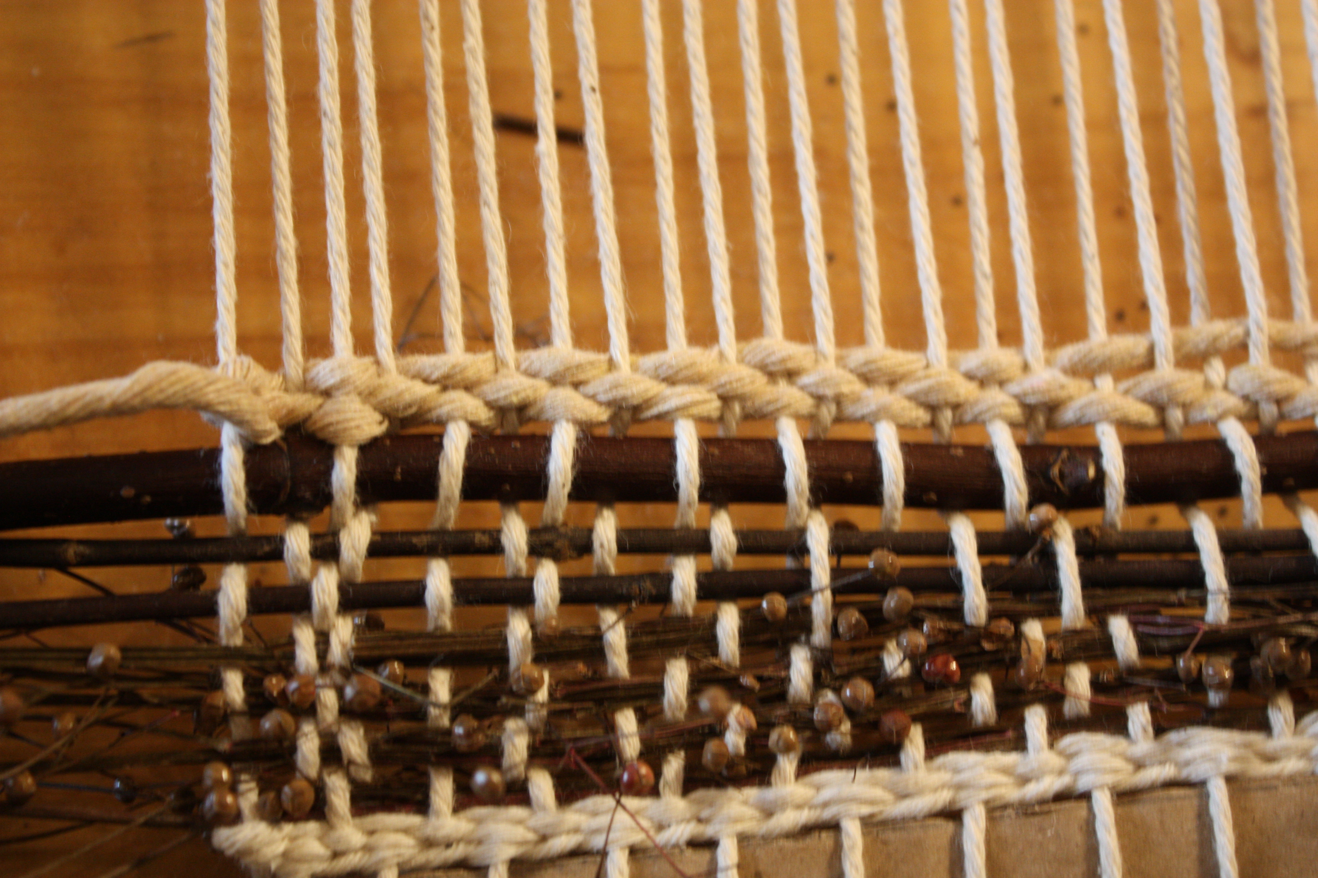  In-progress weaving with natural materials — grasses, twigs, flowers layered between rows of yarn.
