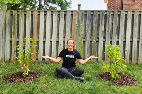 LEAF staff member sitting between two newly planted shrubs