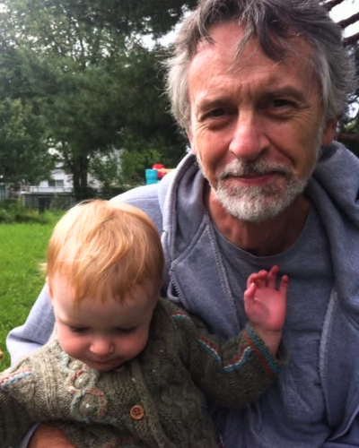 Stuart Grant and a child sitting outdoors in a grassy, tree-filled area.