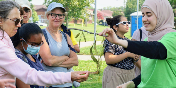 A group of people examining seed pods that a YUFL member in a green LEAF shirt is holding out for them