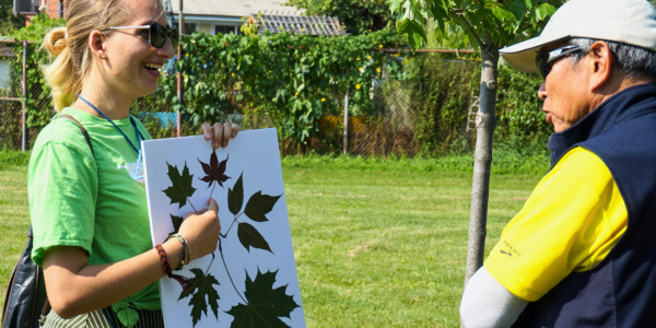 A smiling YUFL member in a green LEAF shirt holding a board with leaves on it to show a tour attendee.