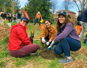 Three volunteers posing with a newly planted tree at a community planting event