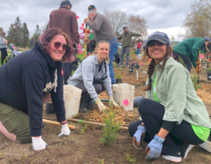 three community members posing while planting a tree at a LEAF community planting event