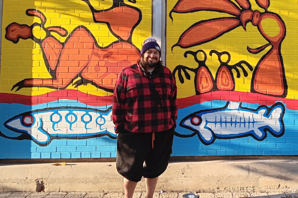 Ojibway Woodland artist Thomas Sinclair posing with his mural, located at the Bathurst Station Urban Forest Demonstration Garden( © 2023 Brian Millward / LEAF)