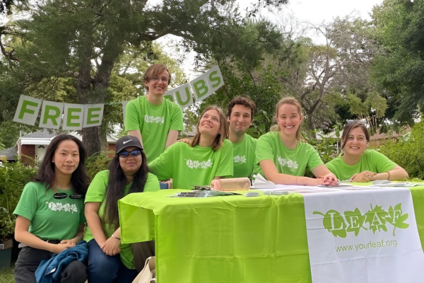 © 2023 Diana Melnikova / LEAF A group of 7 people in green LEAF shirts are sitting at a table smiling at the camera after giving their tree tour
